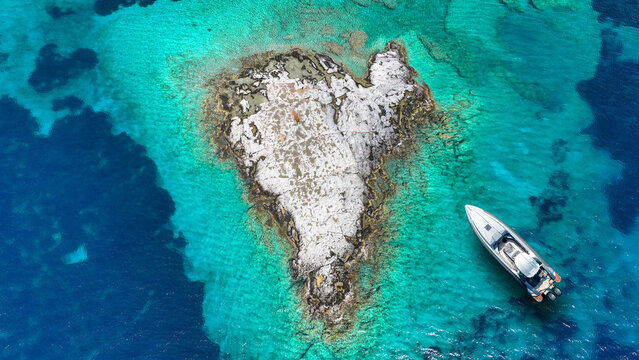 Aerial drone top down photo of inflatable rib anchored in heart shaped small islet of Plaka in Tsigouri beach, Schoinousa, Small Cyclades, Greece