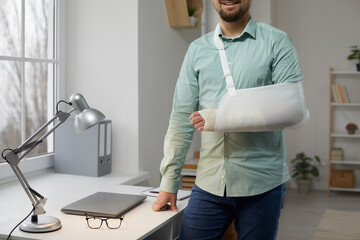 Cropped shot of young man with broken arm in cast. Smiling man wearing an arm splint standing at...