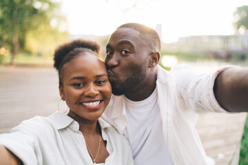 Cheerful black couple taking selfie while sitting on bench in park
