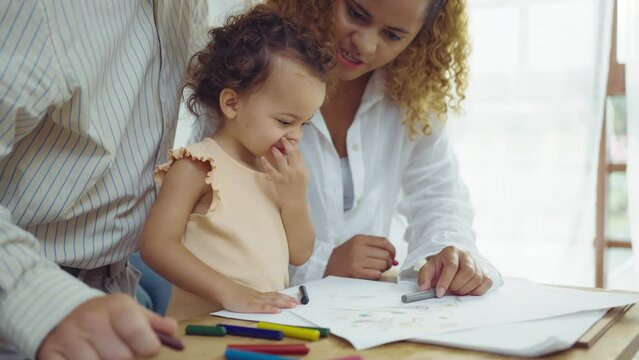 Dad, Mom and little daughter drawing with colorful pencils on paper happy smiling.Young family spend free time together in living room at home.