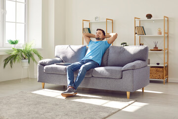 Young relaxed man sitting on comfortable couch in the living room at modern home and having a rest...