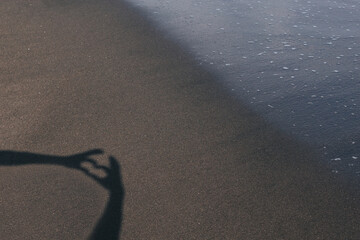 Fototapeta na wymiar Hand gesture in the shape of a heart against the background of a sandy beach. The concept of declaring love on the ocean