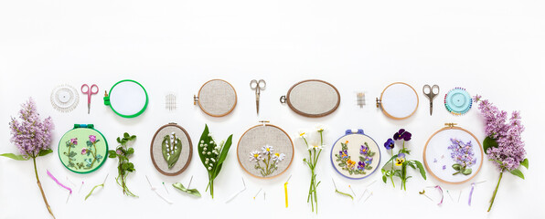 Needlework in summer holidays. Set of hand embroidery with satin ribbons of flowering plants in hoops and fresh flowers on white background. Panoramic view, banner. Flat lay, copy space © Katvic