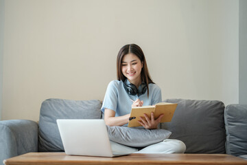 Beautiful asian woman online learning with laptop in living room.