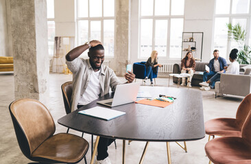 Cheerful black man using mobile phone at creative workspace