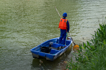 A worker stand in boat to collect garbage in river