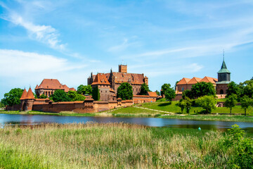 Malbork castle under clear sky during beautiful day with church visibble on the right - obrazy, fototapety, plakaty