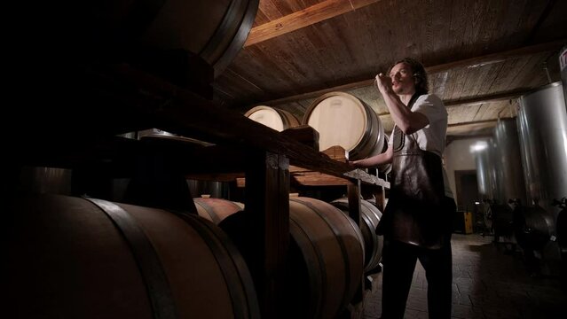 Authentic shot of successful male sommelier is tasting a flavor and checking white wine quality poured in transparent glass in a wine cellar.