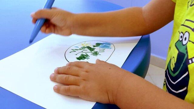 Hands of a Young Preschool Boy Drawing the Earth on White Paper with Blue Color Marker. Occupational Therapy Session.