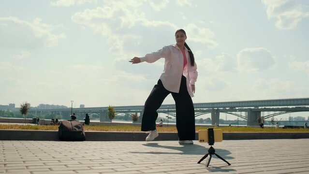 Energetic girl streaming media content using smartphone while dancing on the street