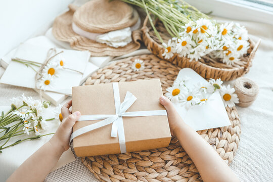 The child's hands hold a beautiful gift box with a ribbon against the backdrop of a festive breakfast. Top view, close-up. Happy mother's day