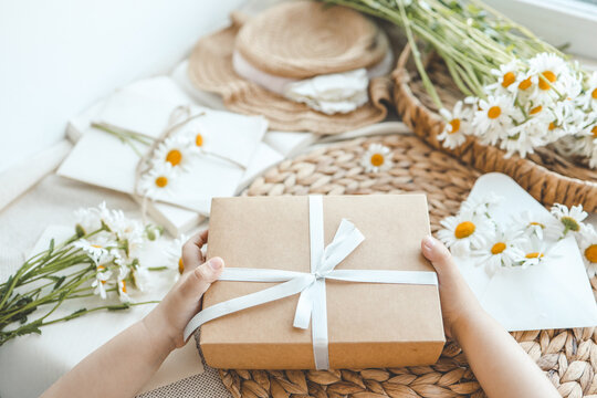 The child's hands hold a beautiful gift box with a ribbon against the backdrop of a festive breakfast. Top view, close-up. Happy mother's day