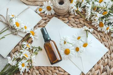 Composition with chamomile flowers and cosmetic bottle of essential oil on white background, top...