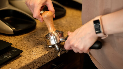 Preparing ground coffee by tamping fresh coffee. Barista hands using tamper to press freshly ground coffee