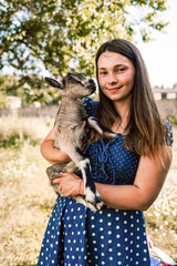 Young woman holding cute baby goat standing near the barn