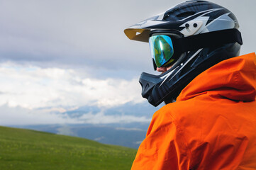 Fototapeta premium Portrait of an unrecognizable male cyclist against the backdrop of clouds and mountains. a man in a full-face helmet with chin protection and mirrored goggles mask looks away