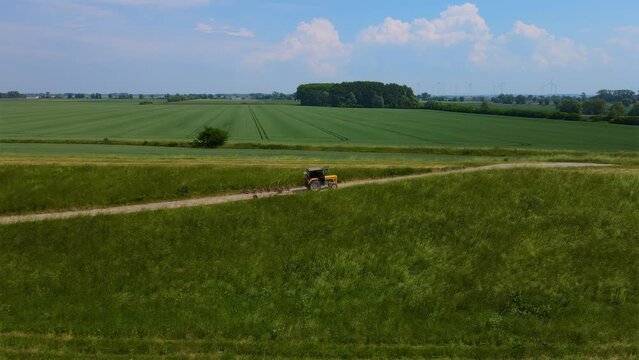 Tractor with hay tedder for drying grass hays driving after agricultural work by rural road. Work in agronomic farm for making business and production organic eco bio animal feed