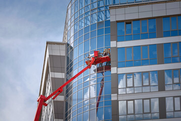 Glass facade cleaning work, workers washing windows at height of high rise building in lifting...