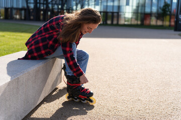 Young pretty woman sitting outdoor and putting on roller blades on a sunny day - obrazy, fototapety, plakaty