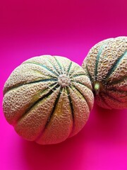 two melons, round melons, retato melon, fruit on a deep pink background, fresh fruit, juicy fruit