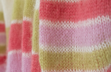Close up of pink, white and green candy striped mohair yarn hand knitted sweater with stitches including stocking stitch and rib, knitted on circular needles. 