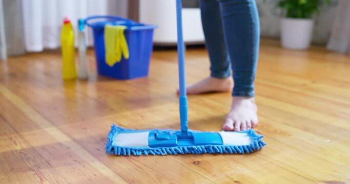 Woman in casual clothes washing a wooden floor with a damp microfiber mop