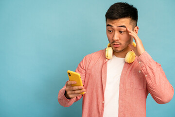 Fototapeta premium Worried man uses mobile phone and rubs his forehead.
