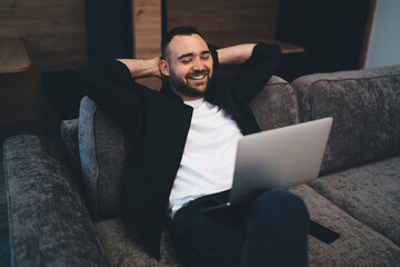 Smiling man with hands behind head looking at laptop screen