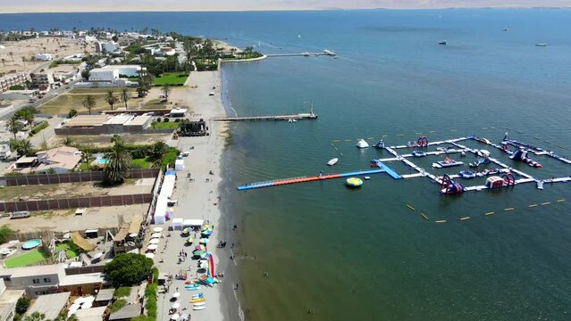 Aerial shot drone slowly descends over beach in Paracas, Peru with inflatable water park