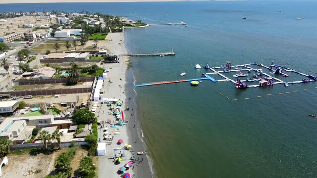 Aerial shot drone flies backwards over beach in Paracas, Peru with inflatable water park