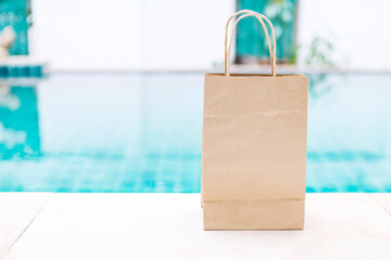 Plain kraft paper bag with handle on swimming pool edge with space on blurred background,...