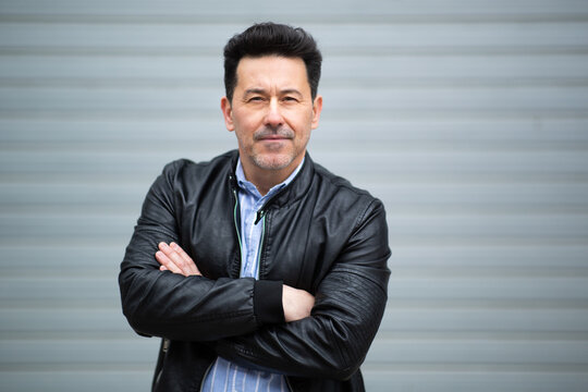 Confident mature man standing with arms crossed against grey background