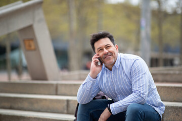 Happy mature man sitting outdoors on steps talking on cell phone