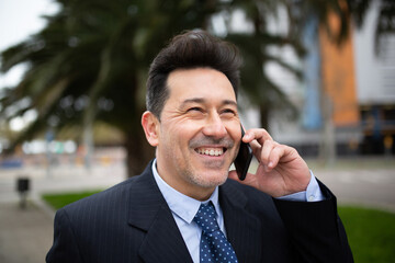 Smiling mature businessman talking on mobile phone standing outside in city