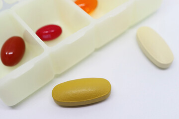 Closeup a Yellow and Off White Pills on White Background with Pill Organizer Case in the Backdrop