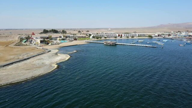Aerial shot drone wide shot flies over water toward pier at edge of boat marina in Paracas, Peru