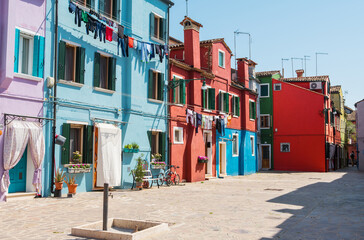 Fototapeta na wymiar Colorful houses along the canal with hinged drying linen on Burano island, Venice, Italy. Attractive famous travel destination.