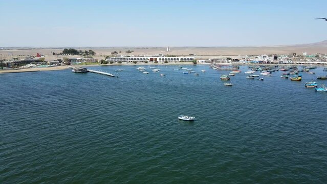 Aerial shot drone flies to the left at a distance from the boat marina in Paracas, Peru