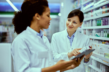 A smiling female pharmacist working with an African female colleague at the tablet.