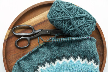 Turquoise green white wool yarn knitting on a needle with yarn ball and vintage scissors,...