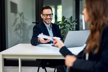 A smiling businessman taking a document from a female colleague at the office.