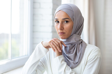 Close-up photo. Portrait of a young beautiful Muslim woman in a white hijab standing indoors by the...