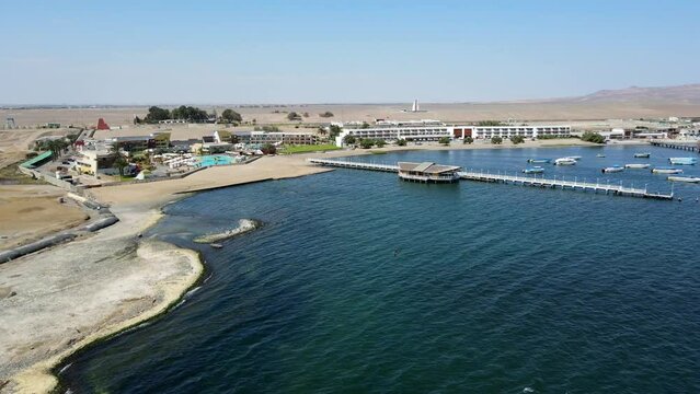 Aerial shot drone medium shot flies over water toward pier at edge of boat marina in Paracas, Peru