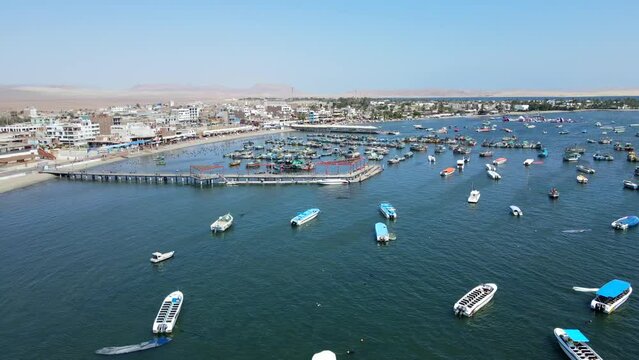 Aerial shot drone flies to the left over boat marina with wooden pier in Paracas, Peru