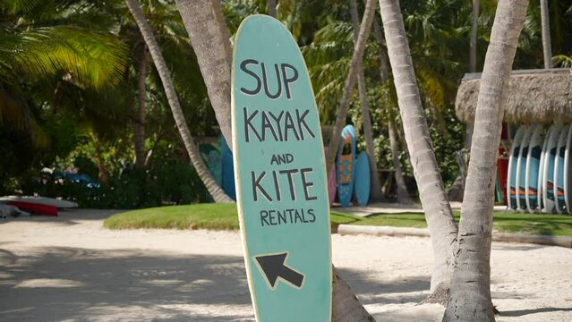 Sign with advertising for rent kitesurfing and kayak on a surfing board in the sand. Activity on the tropical beach on vacation