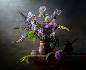 Rustic still life with lupins and irises in a crock on a dark background