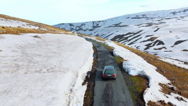 tourists by car climbed high into mountains Armenia, where there snow, view from drone. Mount Aragats, drone follows moving car in snow-capped mountains high. Beautiful landscape from bird's eye view.