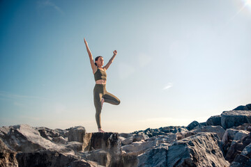 Woman doing a yoga tree pose on top of rocks at sunrise, sunset.