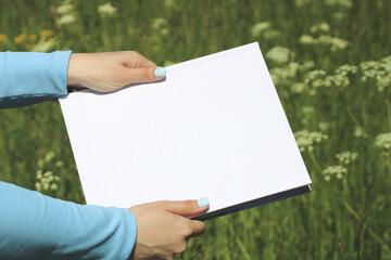 Women's hands hold an album or a book with an empty cover. Mockup, the creator of the scene.