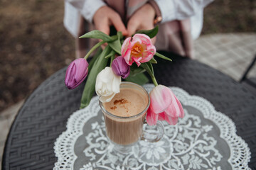 a girl holds a coffee over a table in the middle of tulip flowers 